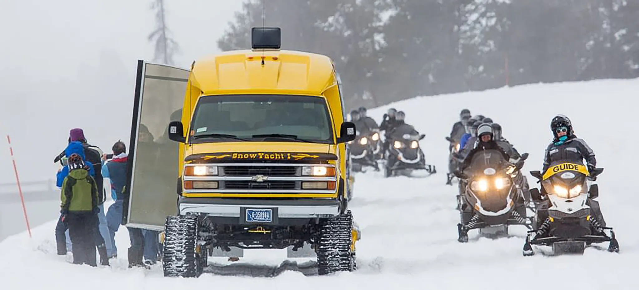 A guided snowmobile group passing a snowcoach on a snowy road